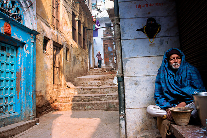 man wrapped in blue shroud sat on wall near steps street photography portrait city people camera subject light how to tutorial guide