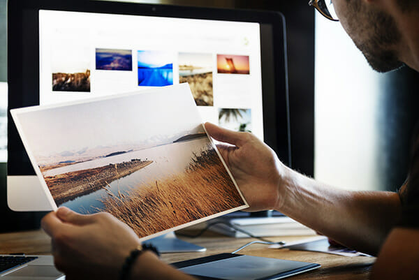 man looking a photograph in front of computer