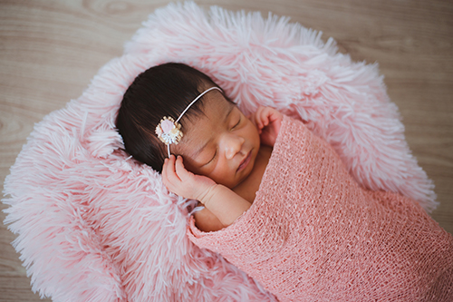 baby asleep lying on a pink fluffy cushion