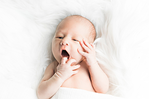 yawning baby lying on white fluffy blanket