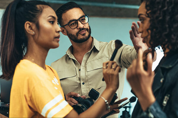 Makeup,Artist,Doing,Makeup,To,A,Model,Using,A,Brush. Makeup artist doing makeup to a model using a brush. Photographer talking to model about the photo shoot. working with models