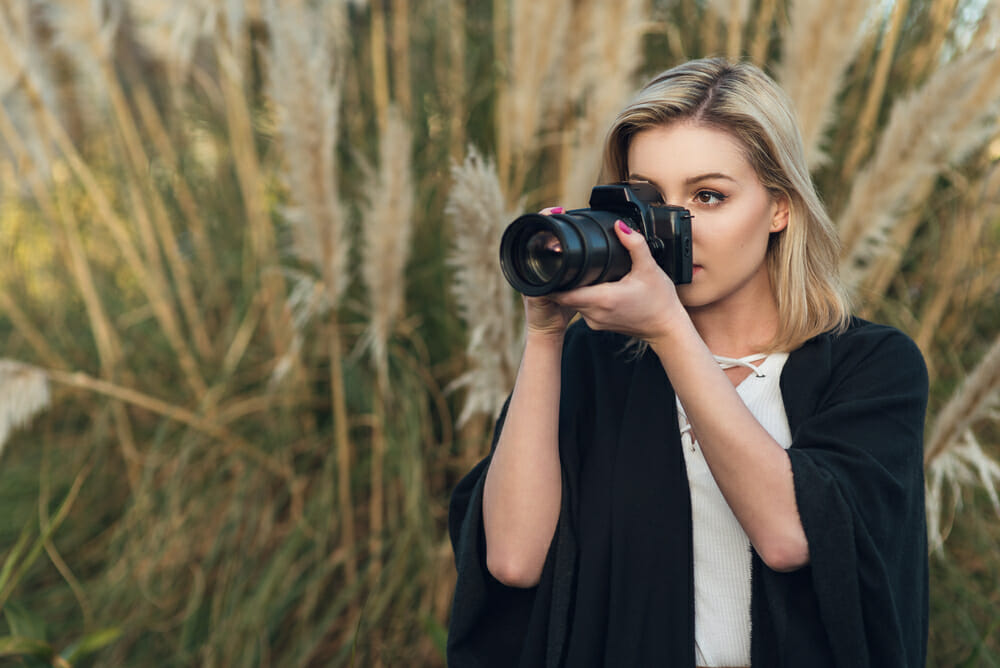 Young,Female,Photographer,Outdoors,With,Digital,Camera,And,Zoom,Lens Female Photographer using a zoom lens to take a photograph